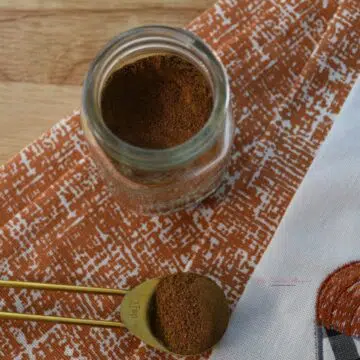 Measuring spoon that has the homemade pumpkin pie spice mixture on it. With more of the spice mixture in a jar.