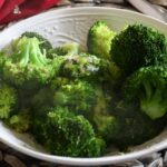 A bowl filled with steamed broccoli with butter on top of it.