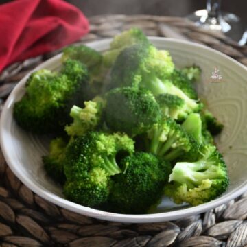A bowl of steamed fresh broccoli with a red napkin behind it.