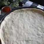 Thin pizza dough on a pan.