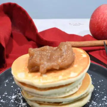 Crockpot pear apple butter on top of pancakes with a cinnamon stick and apple in the background.
