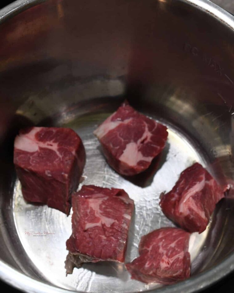 Chunks of chuck roast cut up in the inner pot of an Instant Pot.
