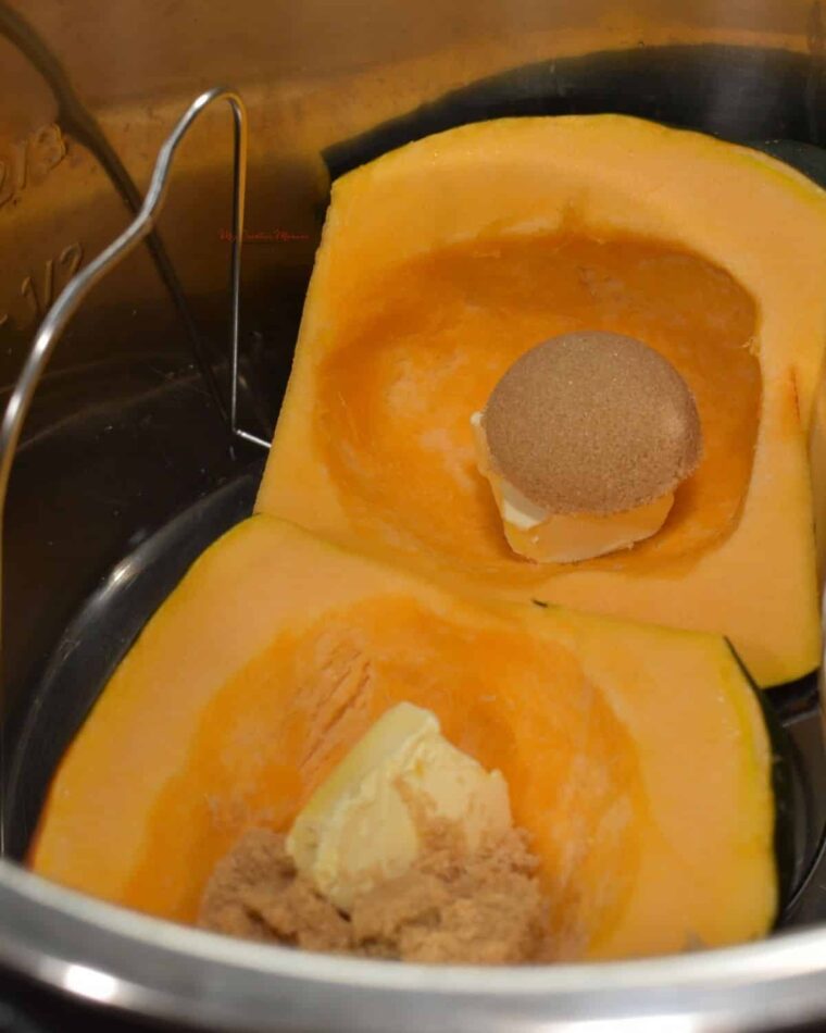 A acorn squash in the inner pot of the Instant Pot with butter and brown sugar in the squash