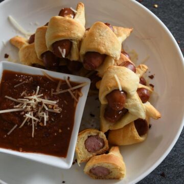 A platter filled with mini pigs in a blanket and pizza sauce.