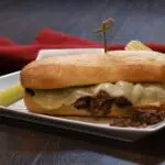 French dip sandwich on a platter with chips and a pickle.