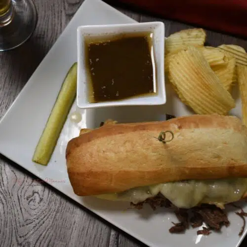 Overhead shot of a sandwich on a platter with a dish of au jus and chips.