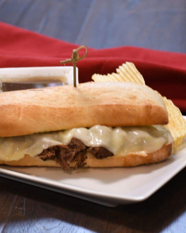 Hoagie sandwich on a platter with chips and au jus sauce.