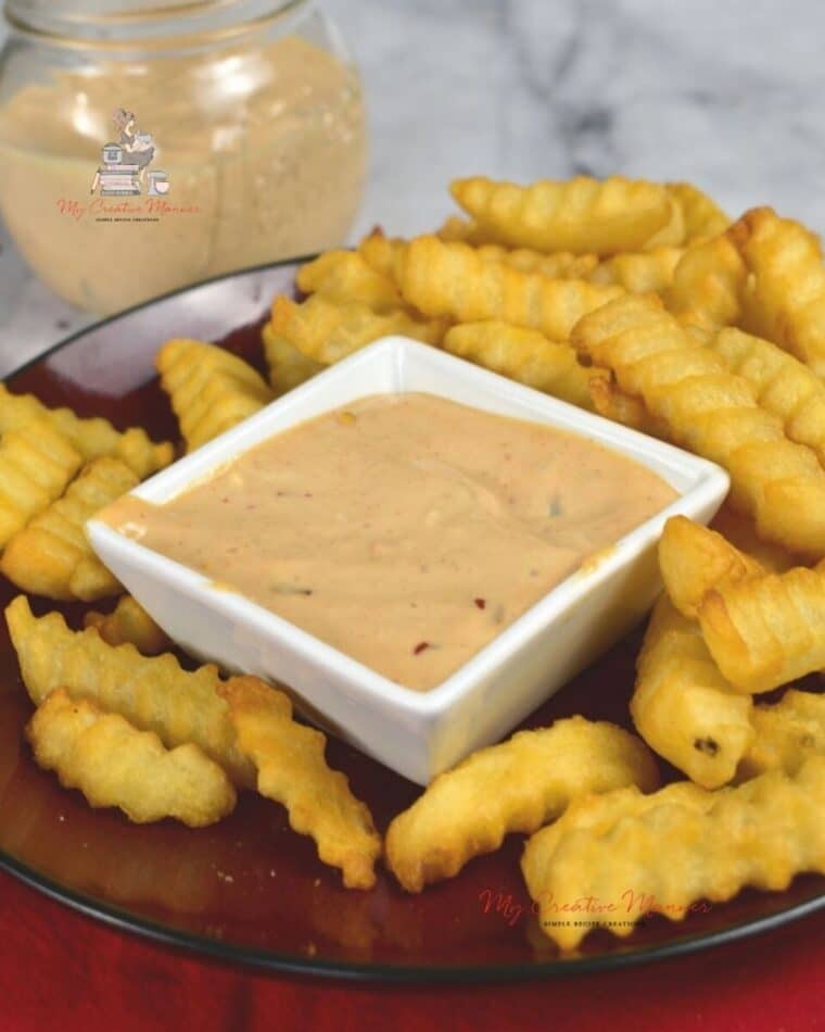 Sriracha dipping sauce in a bowl with French Fries on a white plate.