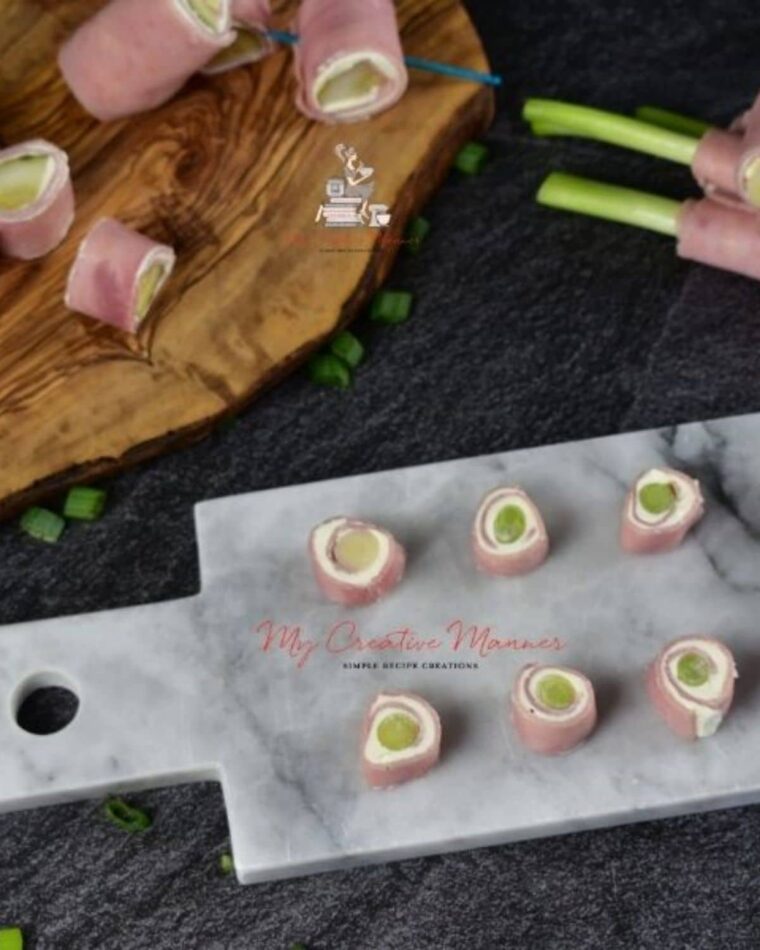 Green onions thata re wrapped in ham and cream cheese sliced on a board.
