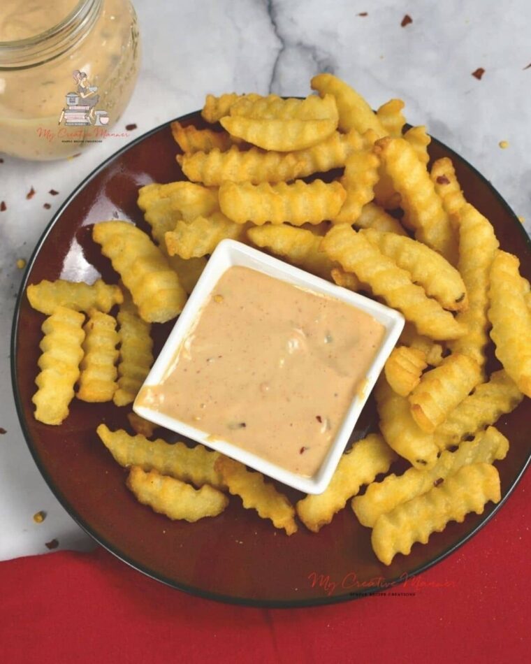 A plate full of French fries with a small dish that has the dipping sauce in it.