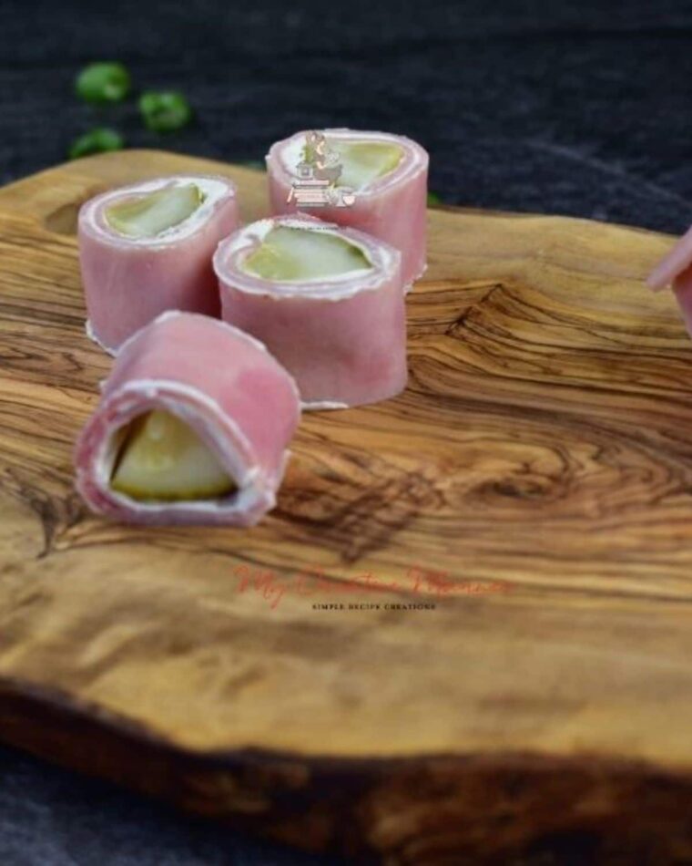 Pickles wrapped in ham and cream cheese on a board.