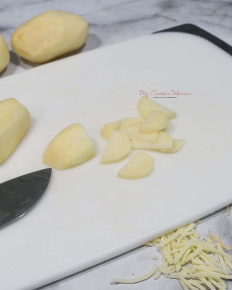 A potato being sliced on a cutting board.