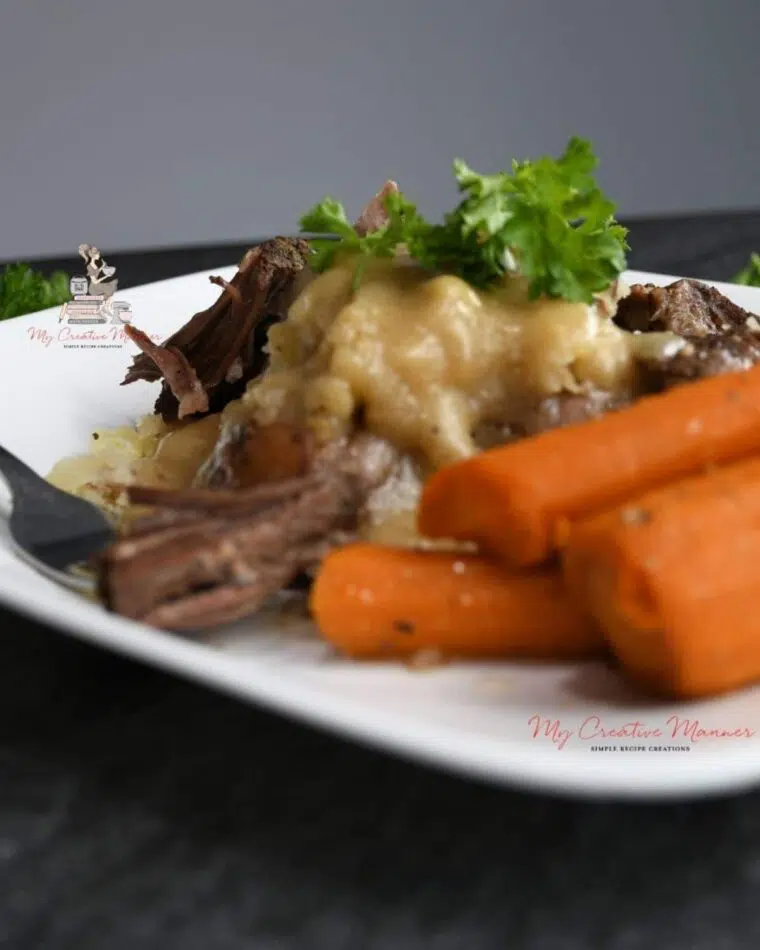 A close up of the slow cooker roast over mashed potatoes with carrots on the side.