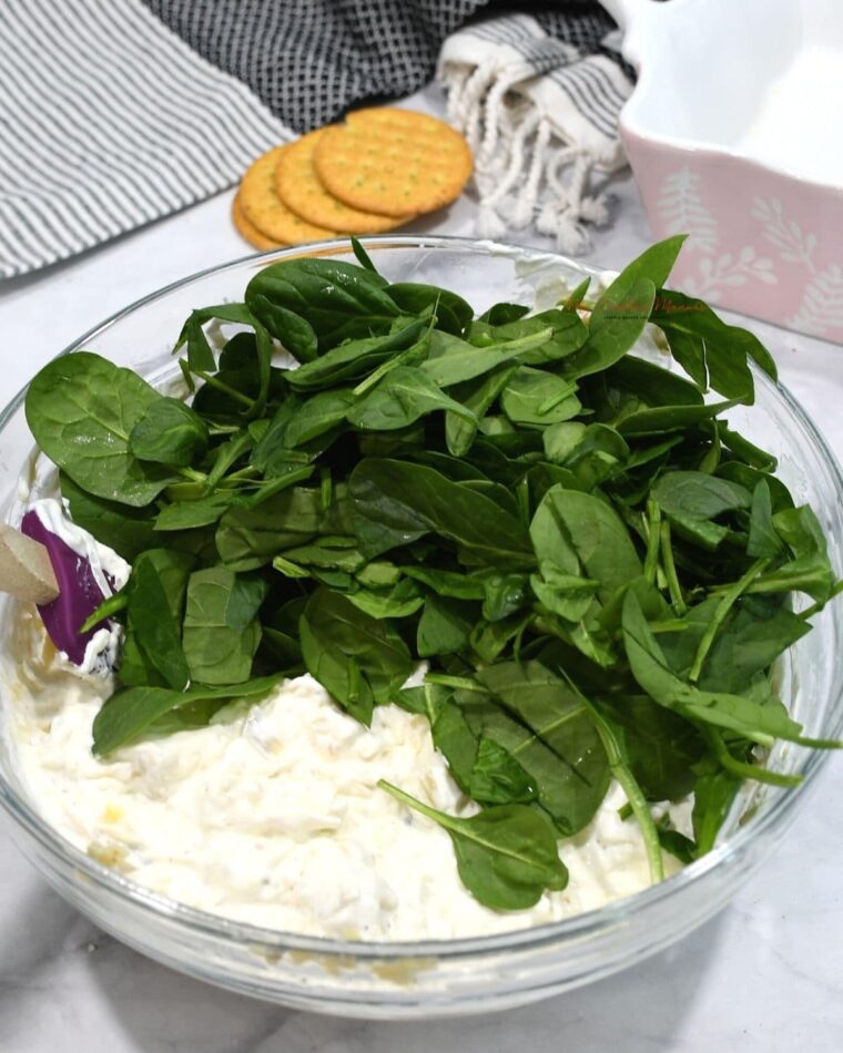 Fresh spinach being added into a cream cheese and sour cream mixture.