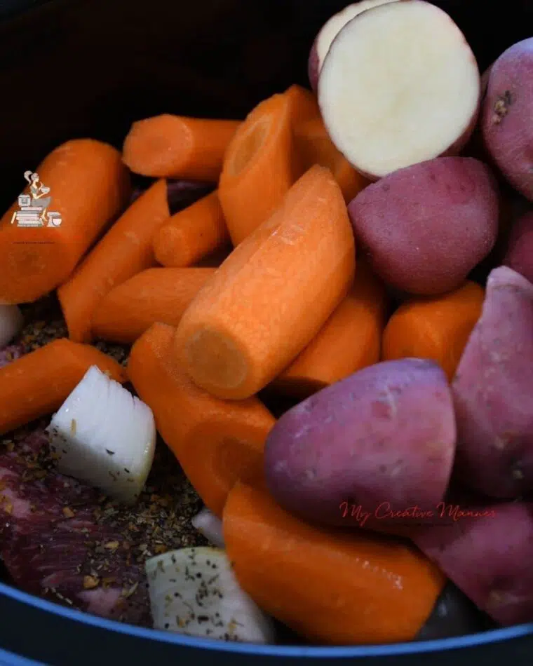 A close of image of carrots, potatoes, and onions in a crockpot.