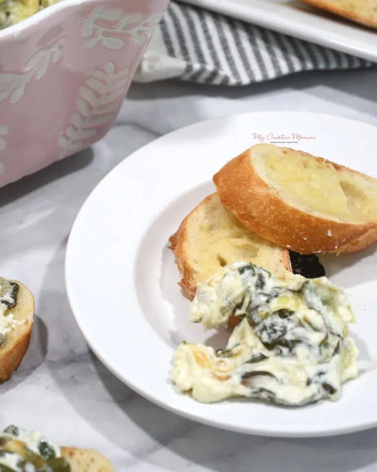 A small white plate with baked spinach artichoke dip recipe and bread slices on it.