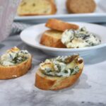 Spinach artichoke dip on bread slices with more on a small white plate.