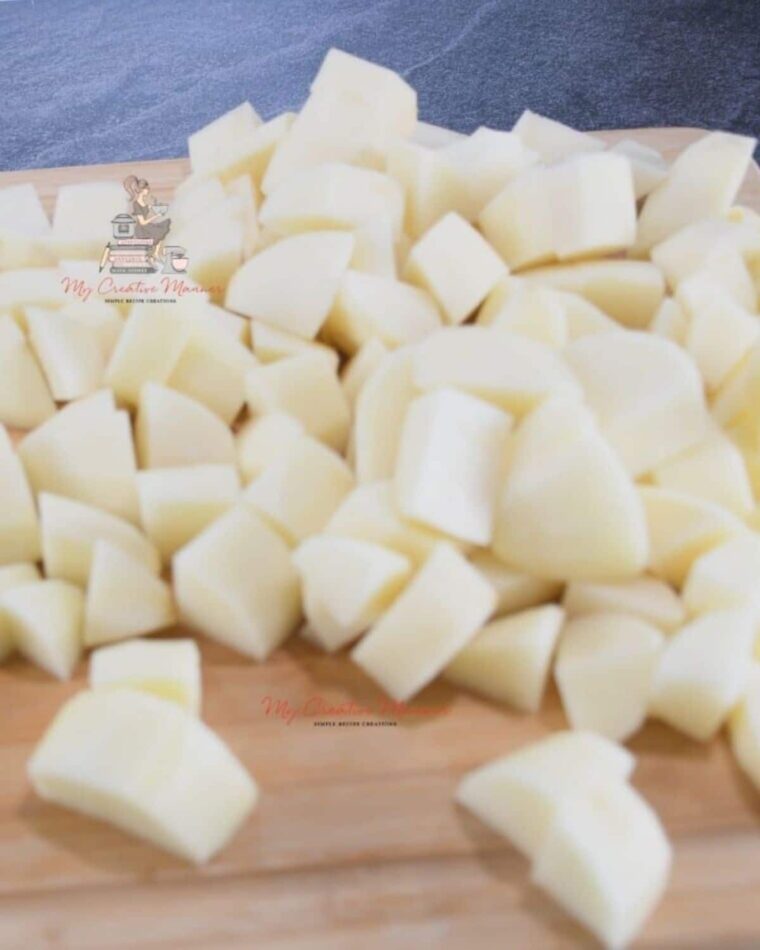 Raw potatoes that are cut up on a cutting board that will be added into a crockpot.