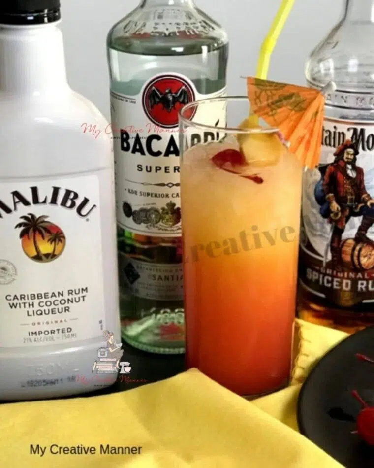 A bahama mama cocktail with a cherry and pineapple in in it. With three bottles of different rums behind it.