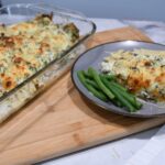 A baking dish with spinach artichoke chicken bake in it. With a plate with chicken breast and green beans on it.