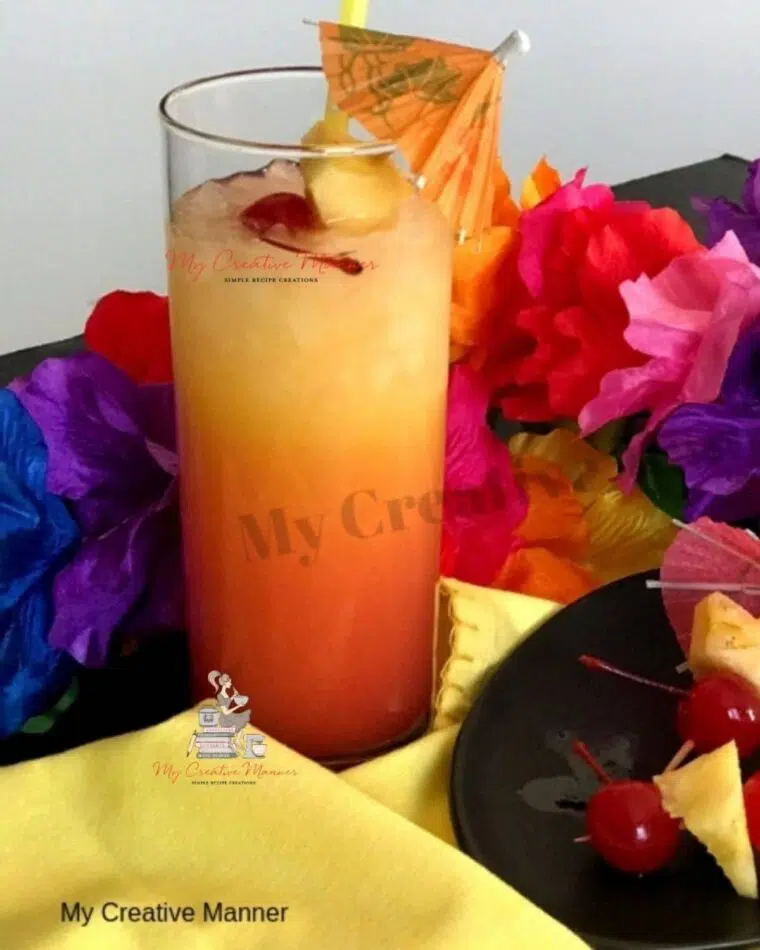 A tall glass filled with a Bahama Mama Cocktail that is made with Captain Morgan. With a plate that has cherries and pineapples on it.