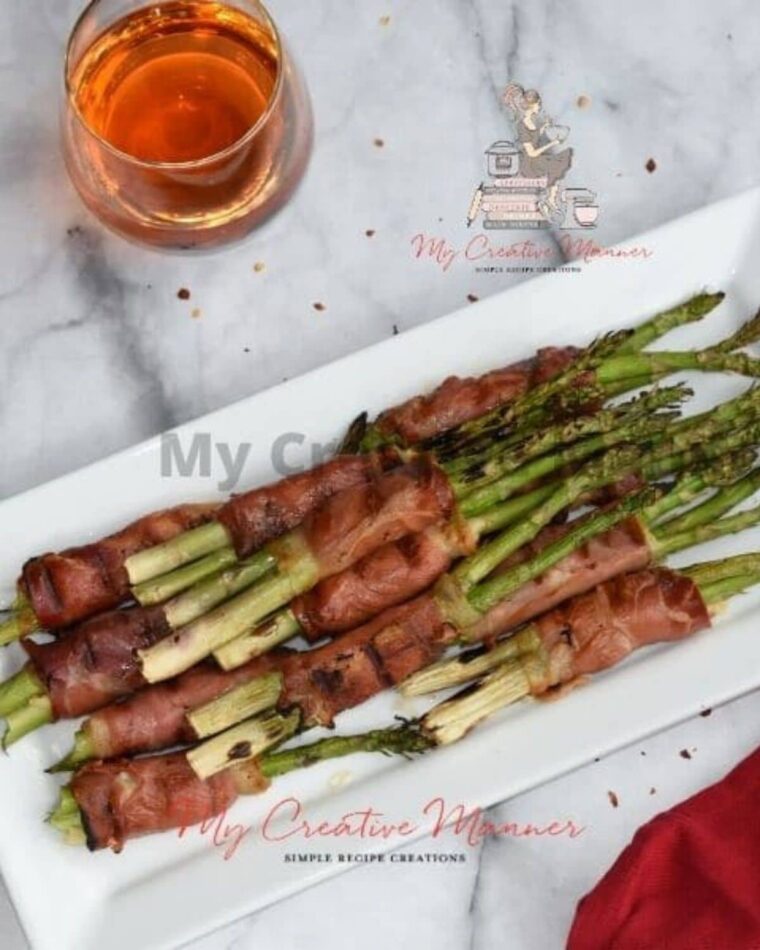 A white plate that has grilled asparagus wrapped with prosciutto and cheese.