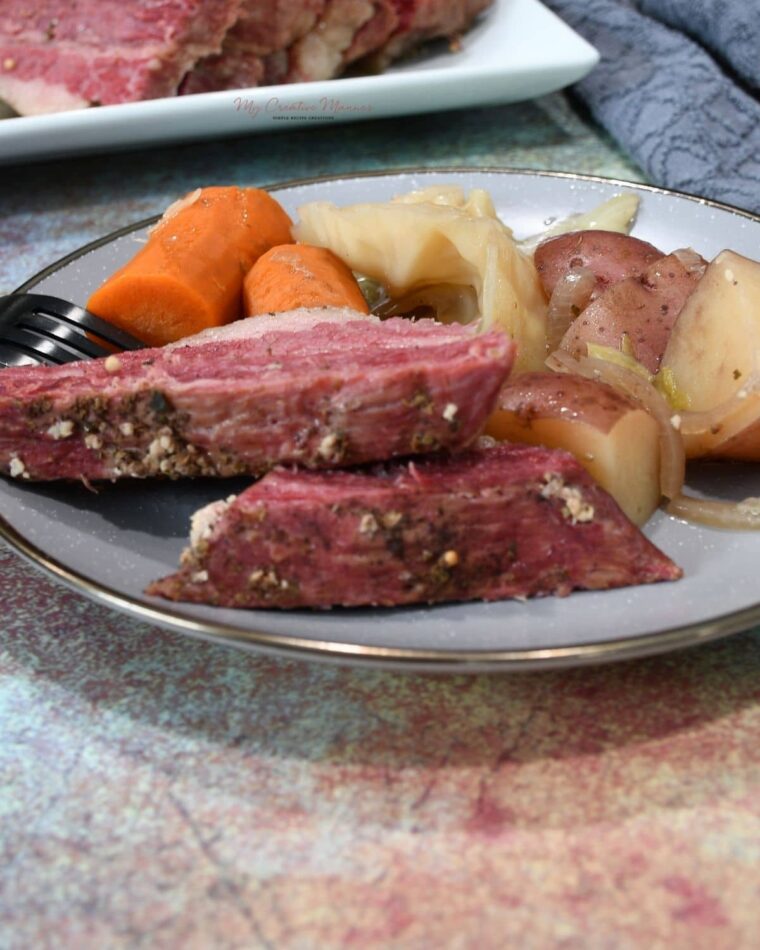 Two slices of corned beef on a plate with vegetables.