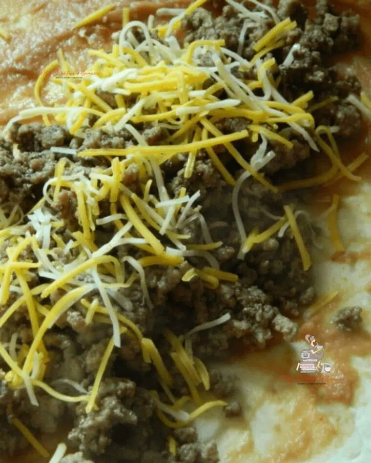 Cooked ground beef topped with cheese on a burrito shell.