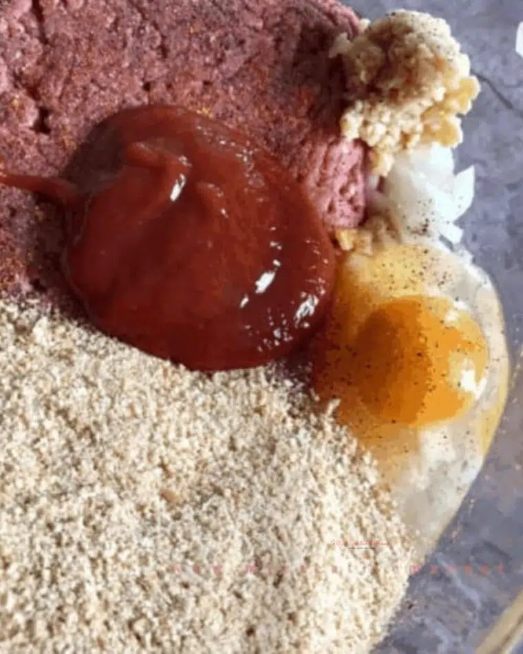 A bowl with ground beef, eggs, garlic, onion,bread crumbs, and some of the glaze recipe.