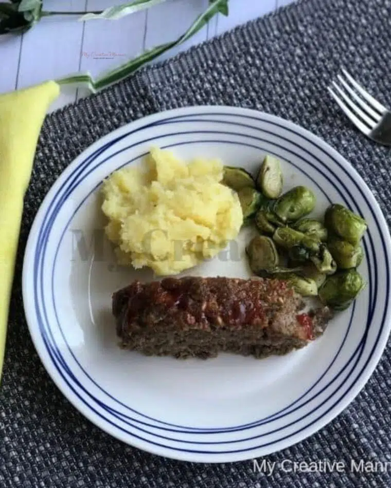 Best Meatloaf recipe with a ketchup glaze.  #mycreativemanner A slice of the best classic meatloaf recipe on a plate with mashed potatoes and Brussel sprouts.