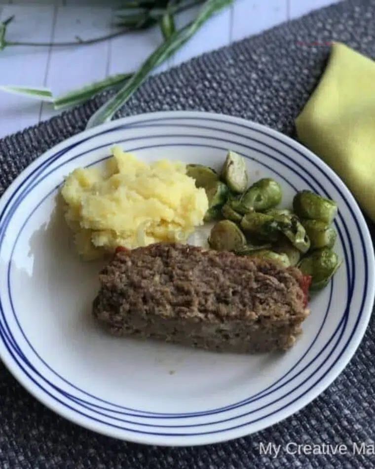 Traditional meatloaf on a plate with mashed potatoes and a vegetable.