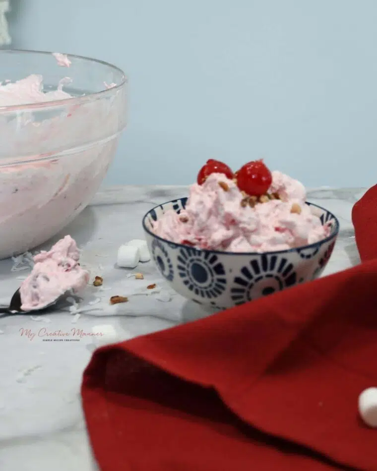 A bowl filled with cherry fluff salad with two cherries on top.
