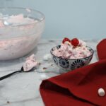 Front view of the cherry fruit salad that's made with cool whip in a small bowl, on a spoon, and more in a larger bowl.