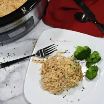 Easy to make crockpot chicken and gravy over mashed potatoes with broccoli on a white plate.