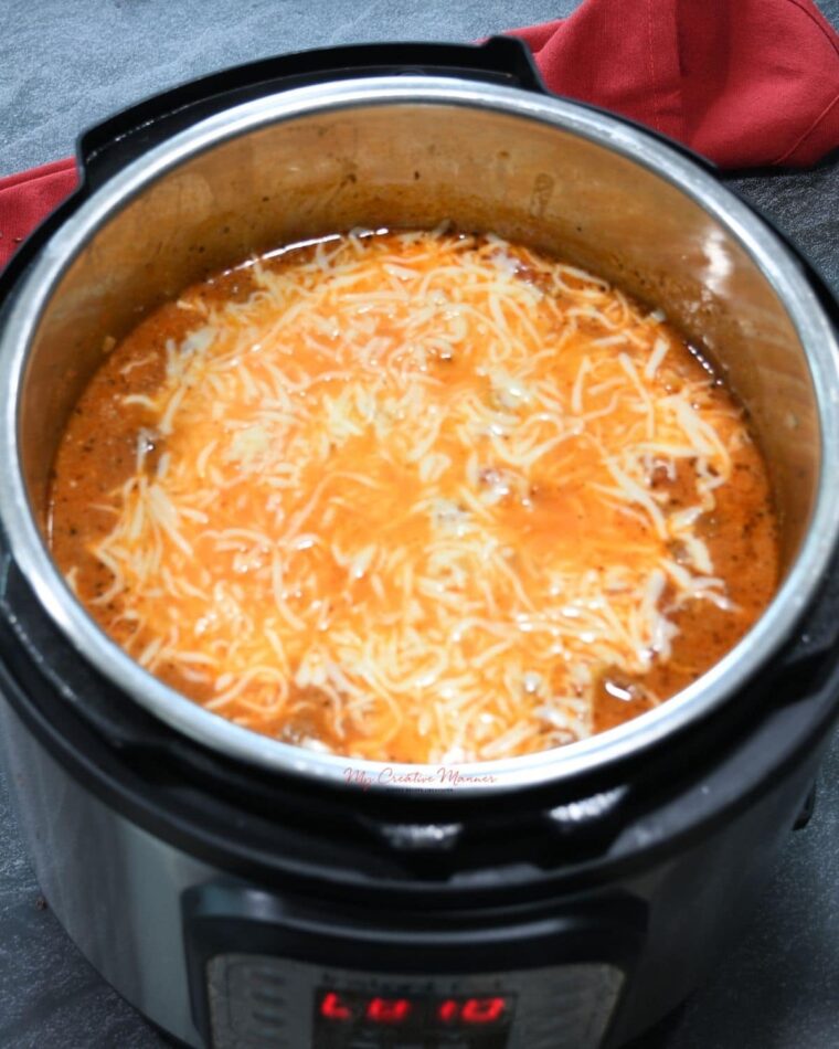 The inner pot of the pressure cooker that is full of the recipe with cheese that is melted on top. 