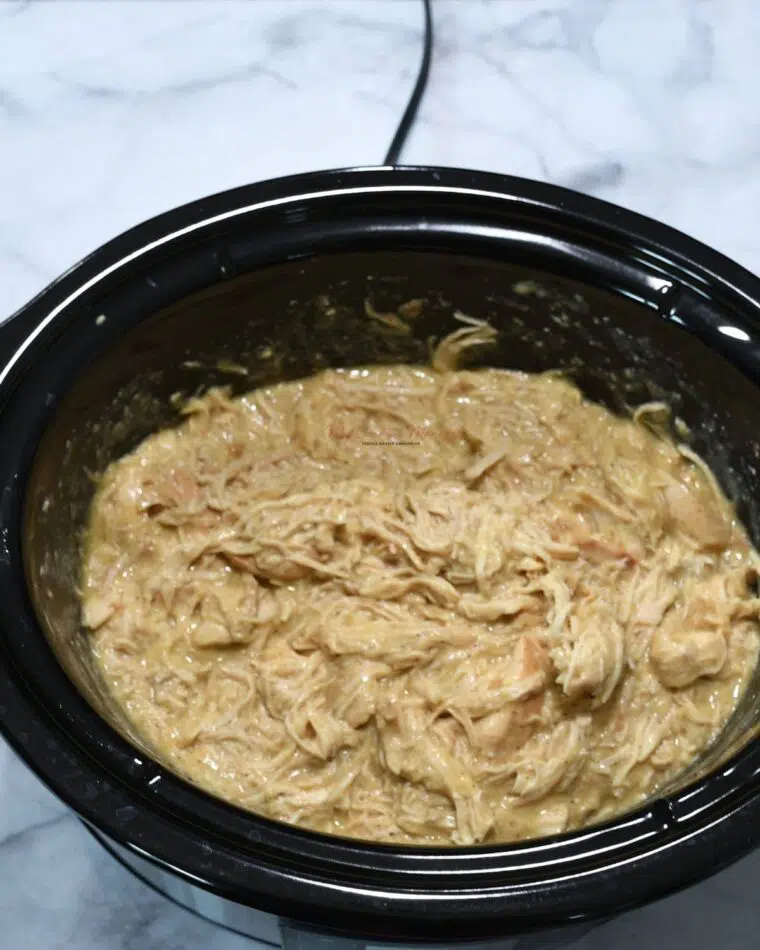 A slow cooker that is filled with shredded chicken and gravy.
