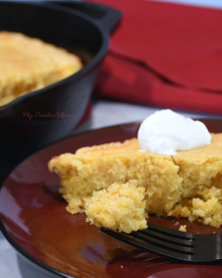 A close up of cast iron skillet cornbread with creamed corn on a fork with more on a plate.