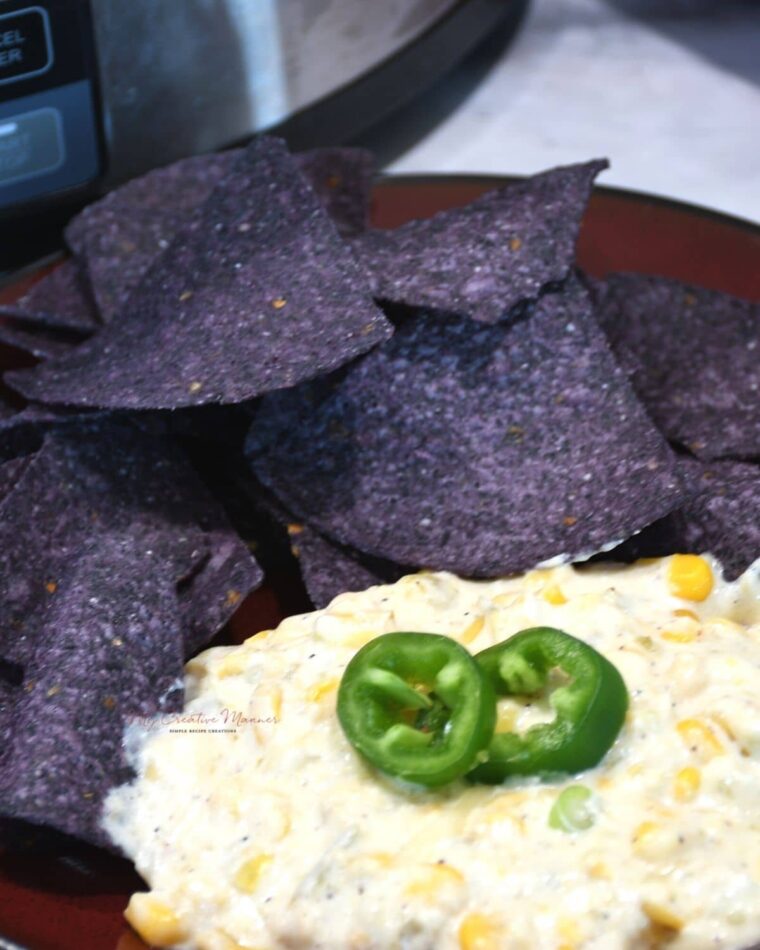 A close up of corn dip on a plate with tortilla chips.
