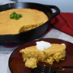 A close up of cornbread on a plate and more in a skillet behind the plate.