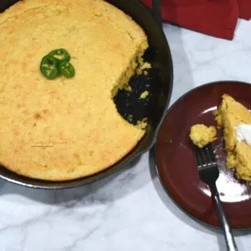 Overhead image of a cast iron skillet with cornbread with creamed corn in it. More of this easy cornbread recipe in a cast iron skillet next to the plate.