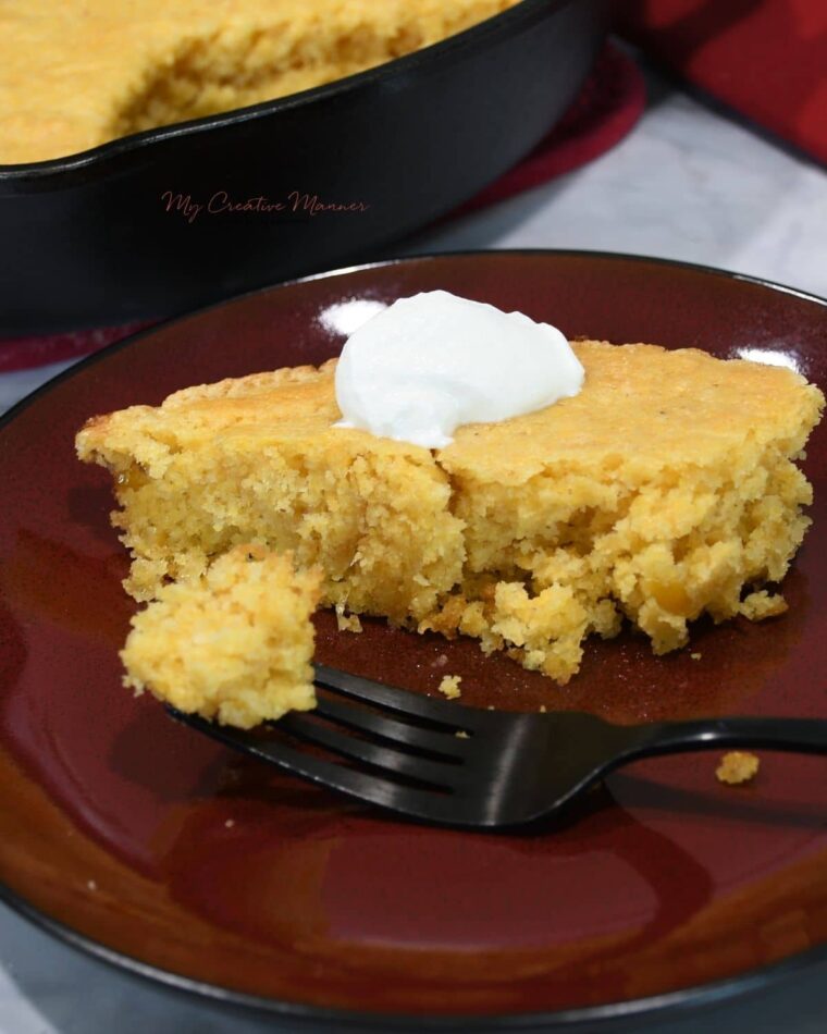 Cornbread made with creamed corn on a plate with a dollop of sour cream on top of the cornbread.