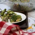 A close up of broccoli salad with bacon and cranberries on a plate with more in a bowl behind the plate.