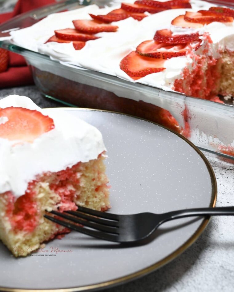 A slice of jello poke cake that is topped with cool whip and fresh strawberry.