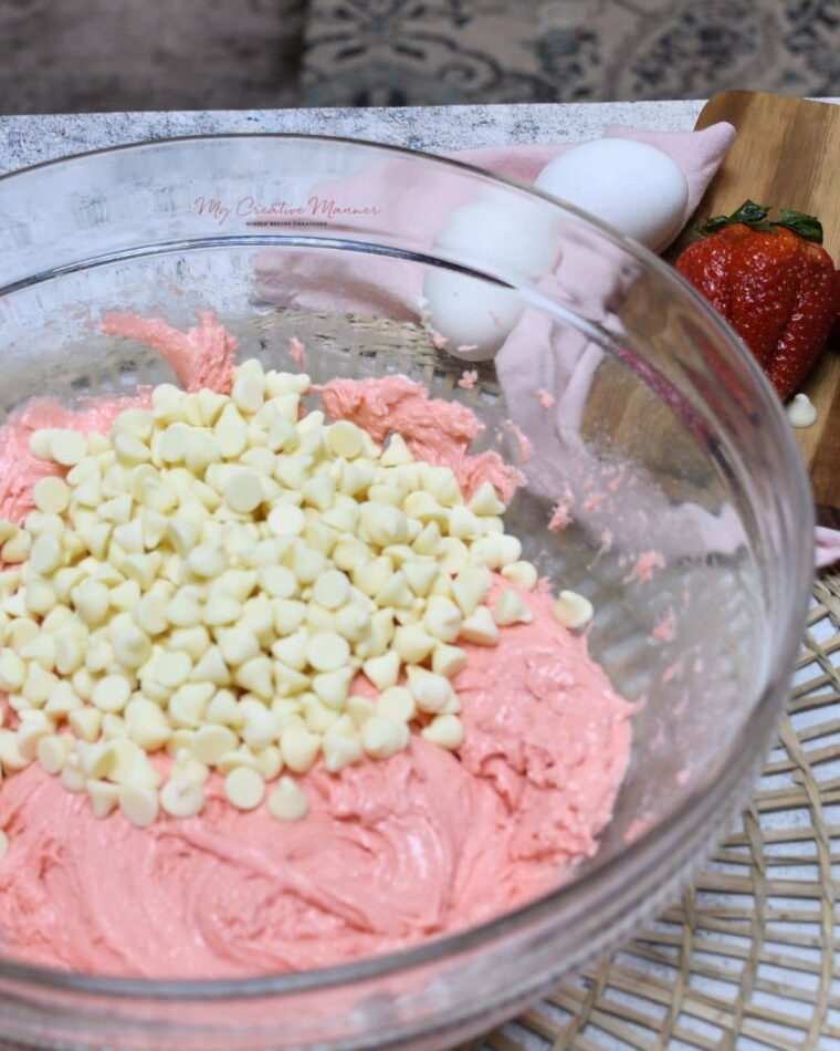 A bowl with the cake batter mixed up with white chocolate chip in it ready to make strawberry cookies.
