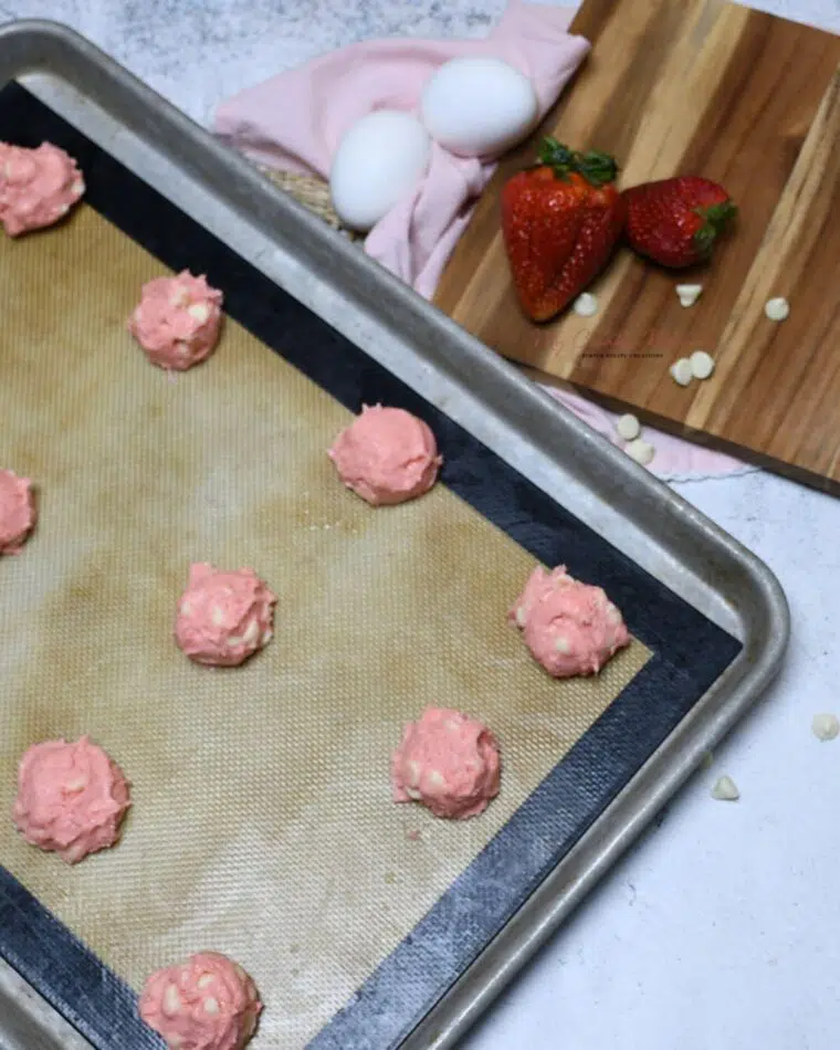 A cookies pan with unbaked strawberry cake cookies with white chocolate on it.