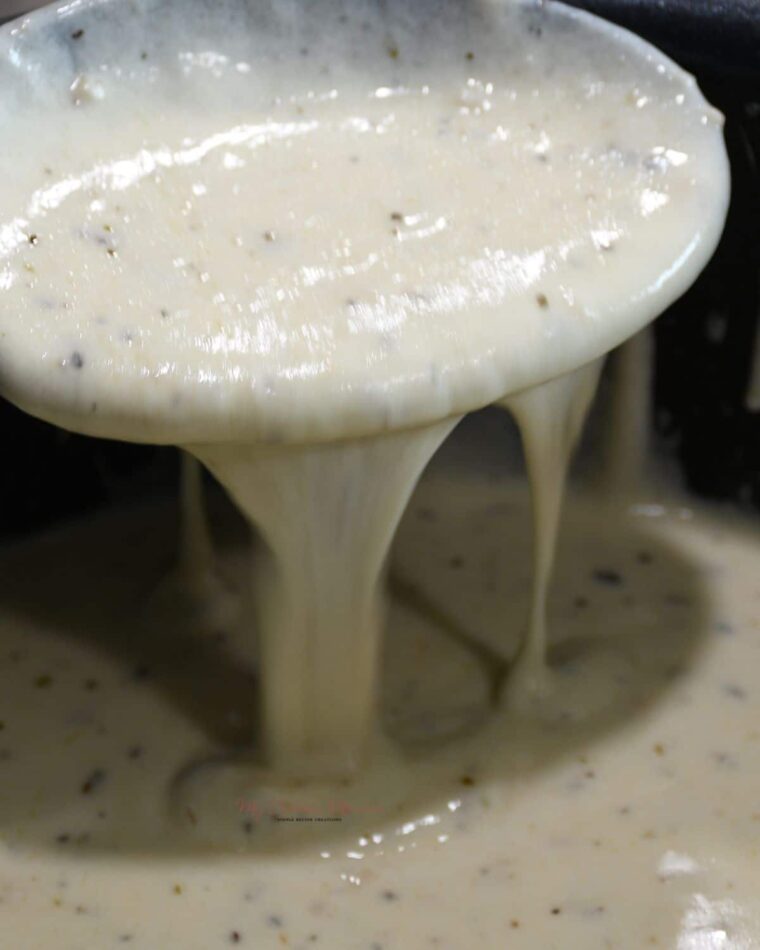 A close up of creamy white alfredo sauce with heavy cream dripping off a spoon.