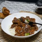 A front view of a dish that has crockpot Mongolian beef with a fork.