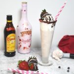 A tall glass filled with a frozen strawberry mudslide drink. A bottle of Kahlua and Bailey's is behind the glass with fresh strawberries.