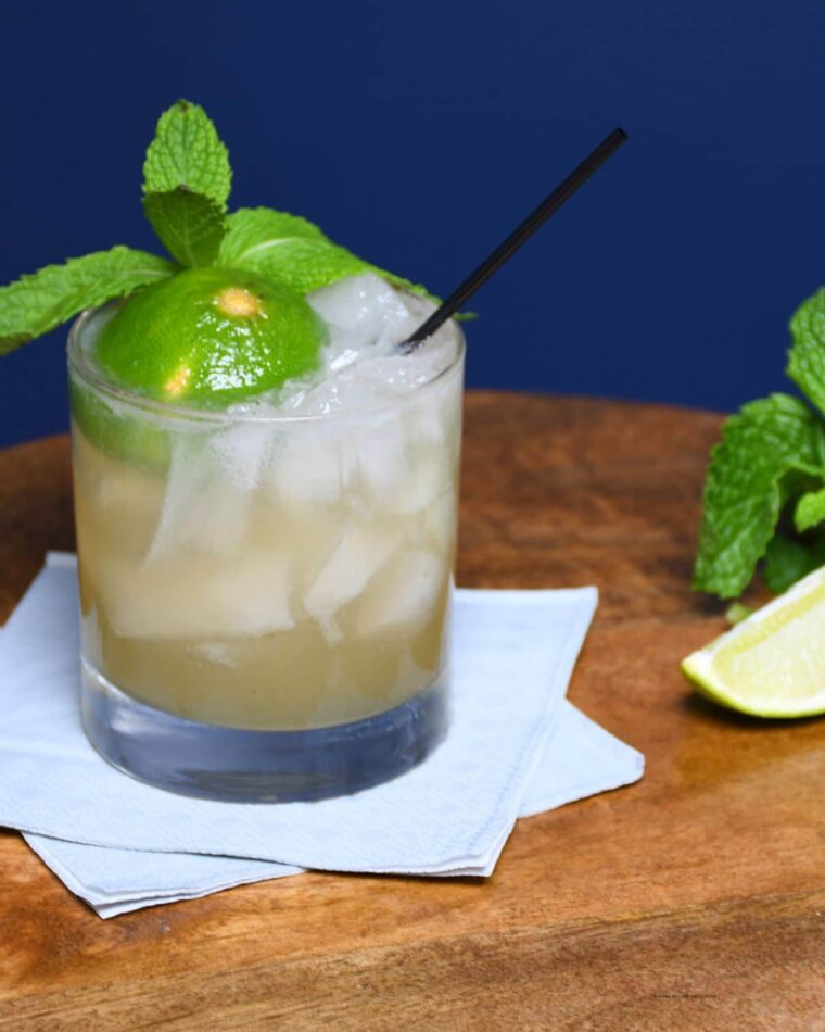 A small glass with filled with the original mai tai cocktail recipe. A lime and mint springs are the garnish for this cocktail recipe.