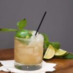 A close up of a glass that has the original recipe for a mai tai in it. The cocktail recipe is garnished with a half of lime and a spring of mint.